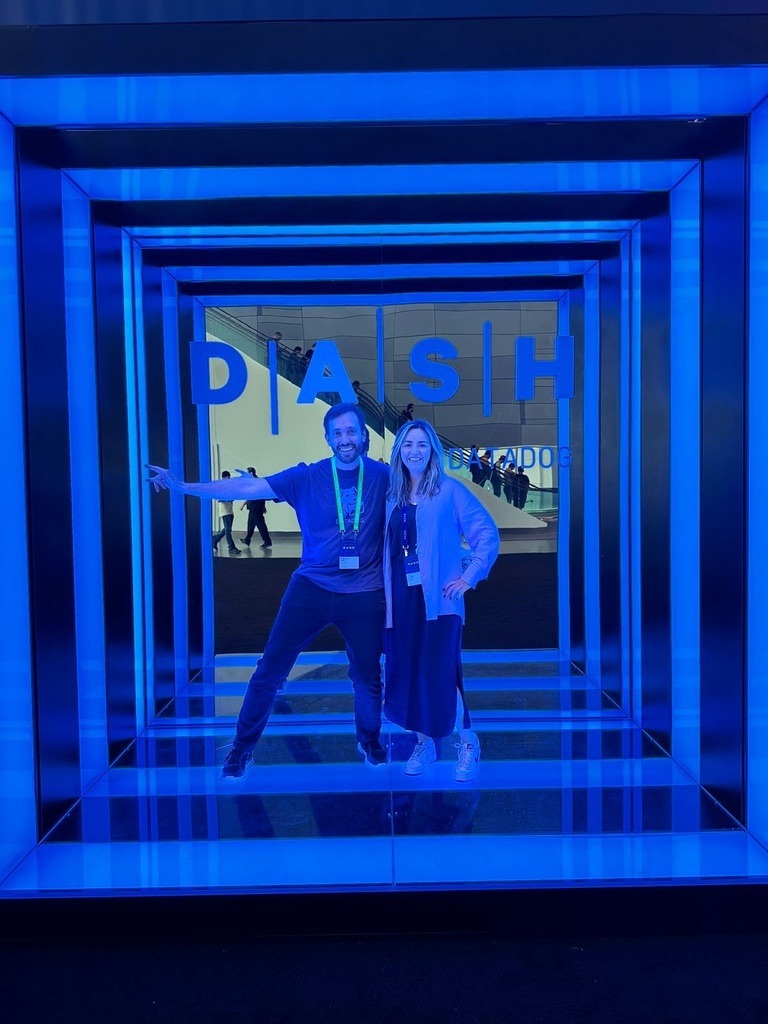 Federico Toledo and Lina Giraldo standing together in front of a blue-lit DASH by Datadog sign at a conference event.